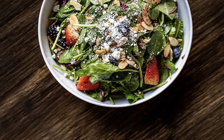Overhead view of a colorful spinach salad with berries, cheese, almonds.