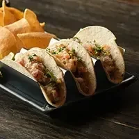 Three tacos in a black metal holder on a dark wood surface.