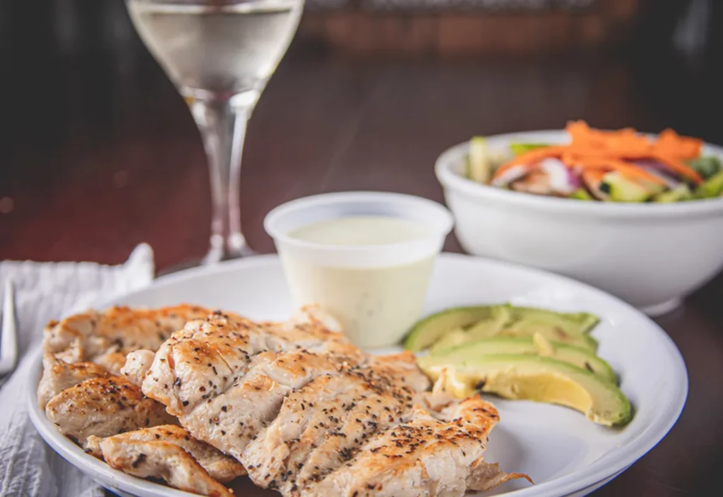 Grilled chicken and avocado meal with salad and wine.