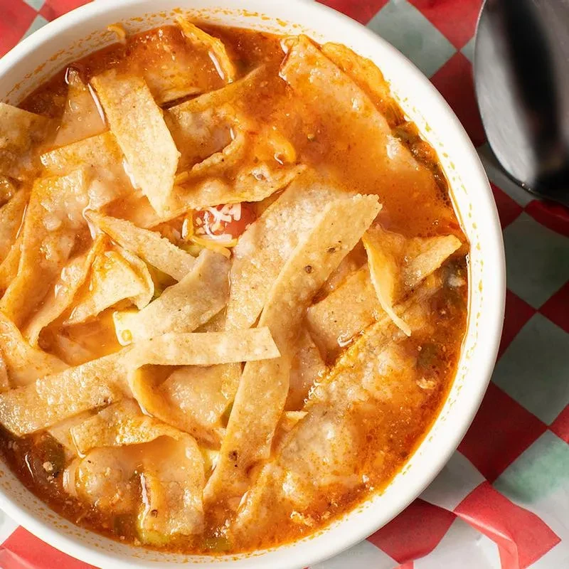 Overhead shot of a bowl of tortilla soup on a checkered tablecloth.