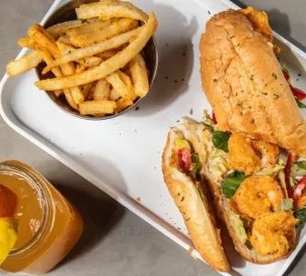 Overhead shot of a fried shrimp po'boy, fries, and a drink.