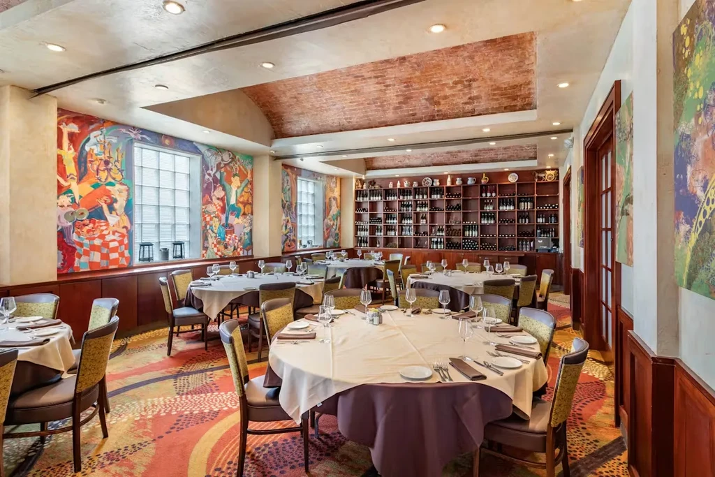 Elegant restaurant dining area with set tables, murals, and wine shelves.
