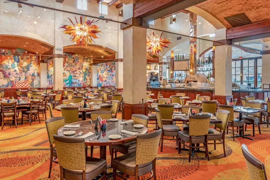Interior of a spacious, upscale restaurant with colorful murals and chandeliers.