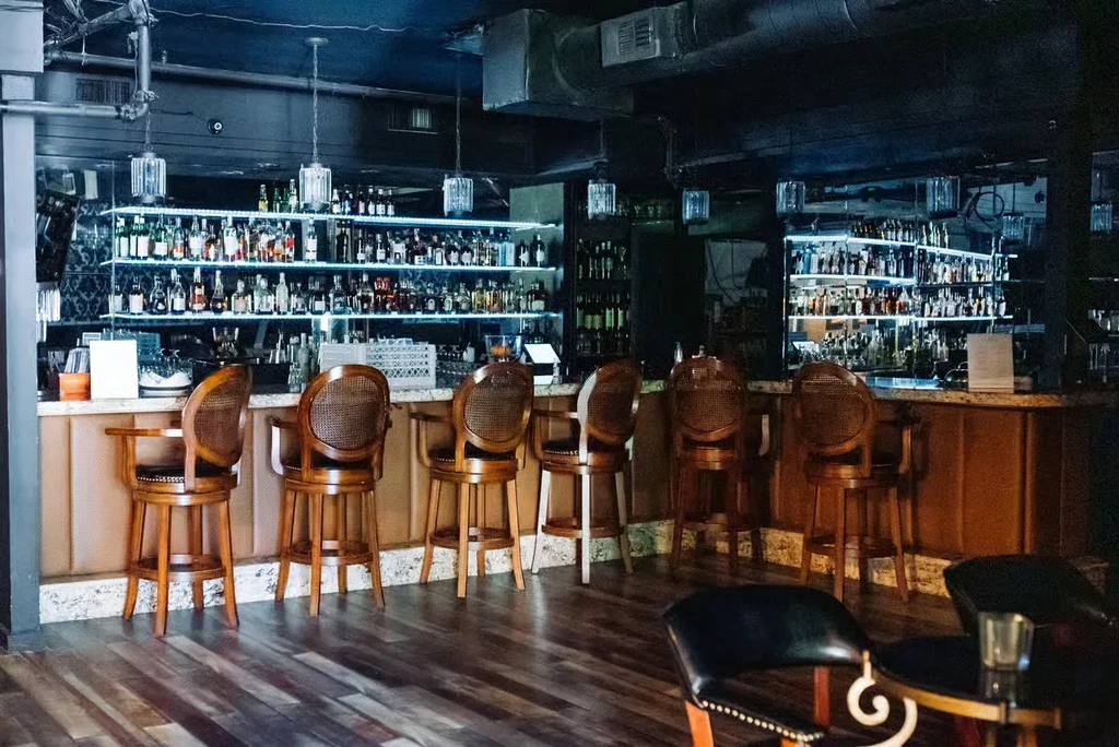 Well-stocked, dimly lit bar with six wooden bar stools.