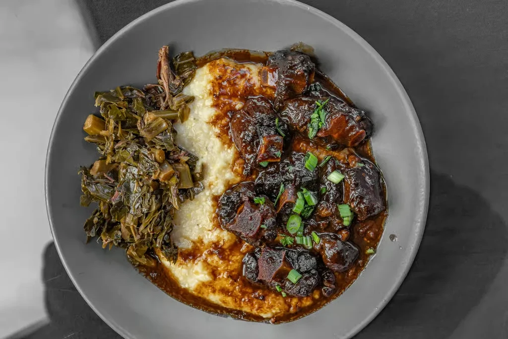 Top-down view of a bowl of grits, stew, and collard greens.