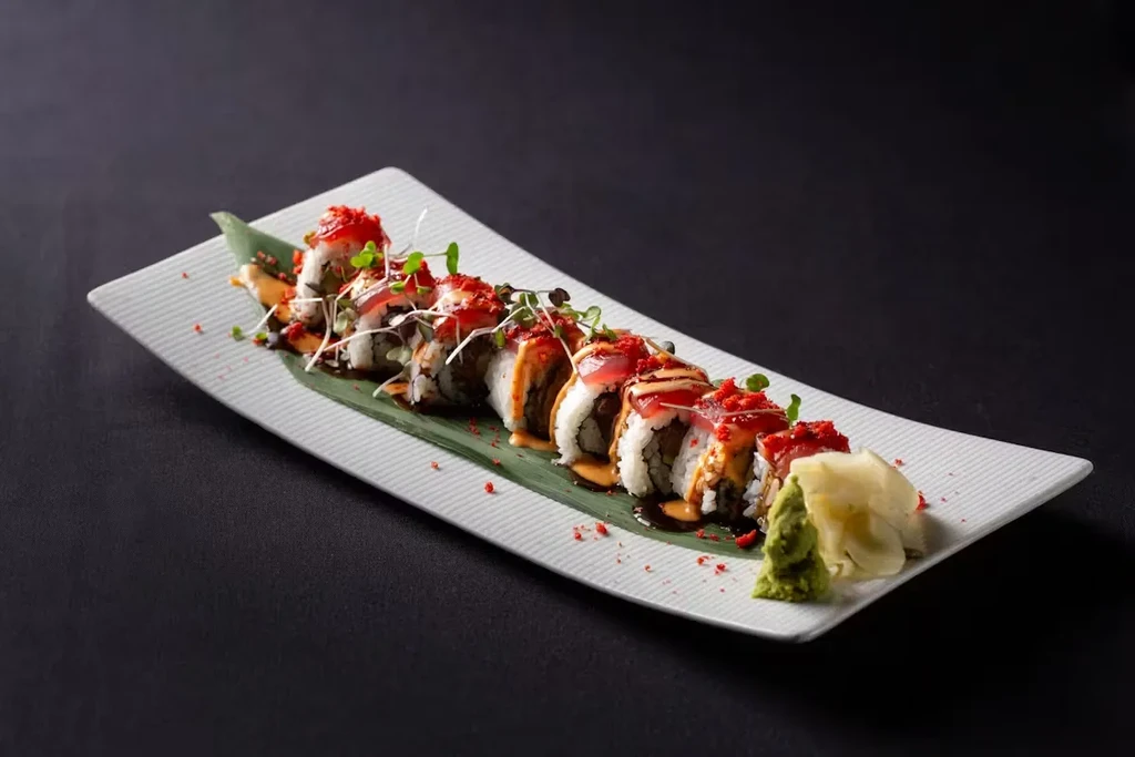 Sushi roll on rectangular white dish with wasabi and ginger.