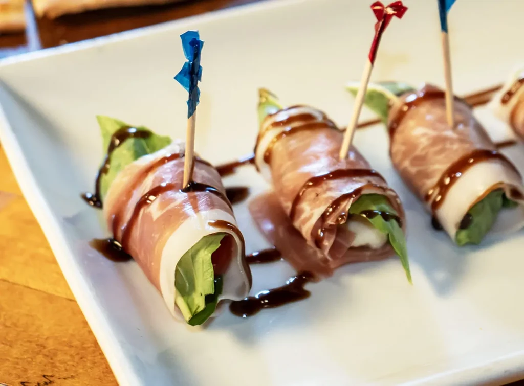 Prosciutto, mozzarella, and basil appetizers on a white plate.