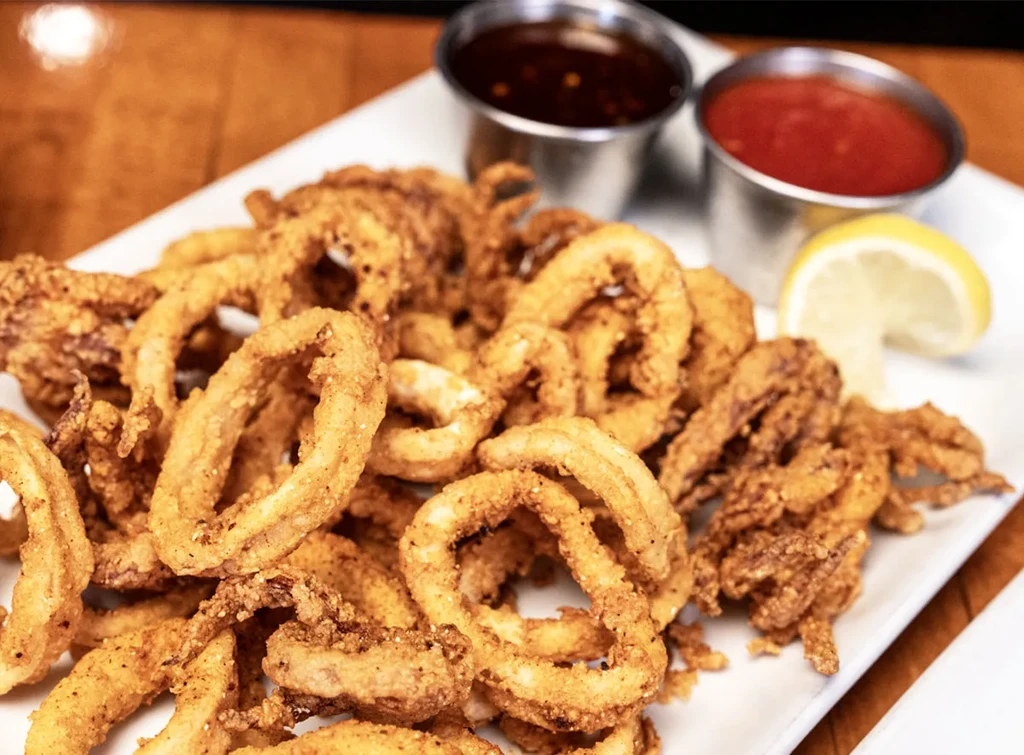 Crispy fried calamari with two dipping sauces and a lemon wedge.