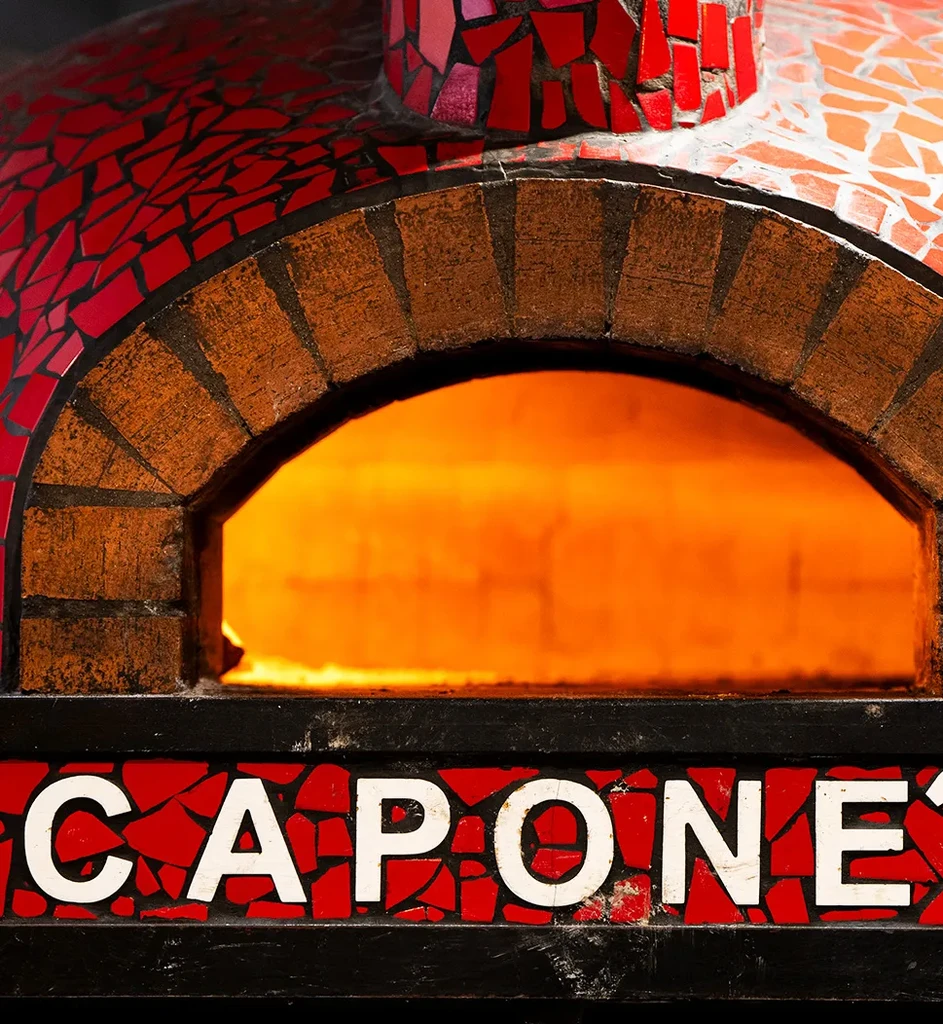 Red mosaic pizza oven with arched brick opening and "CAPONE" text.