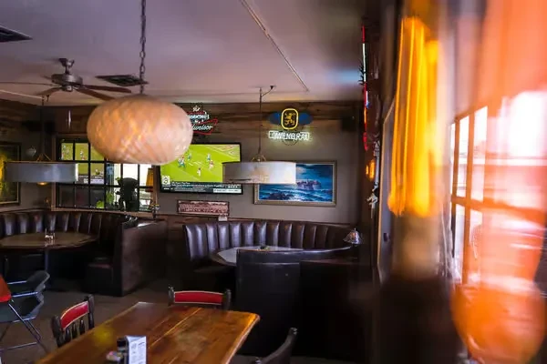 Dimly lit bar interior with booth seating, TVs, and neon signs.