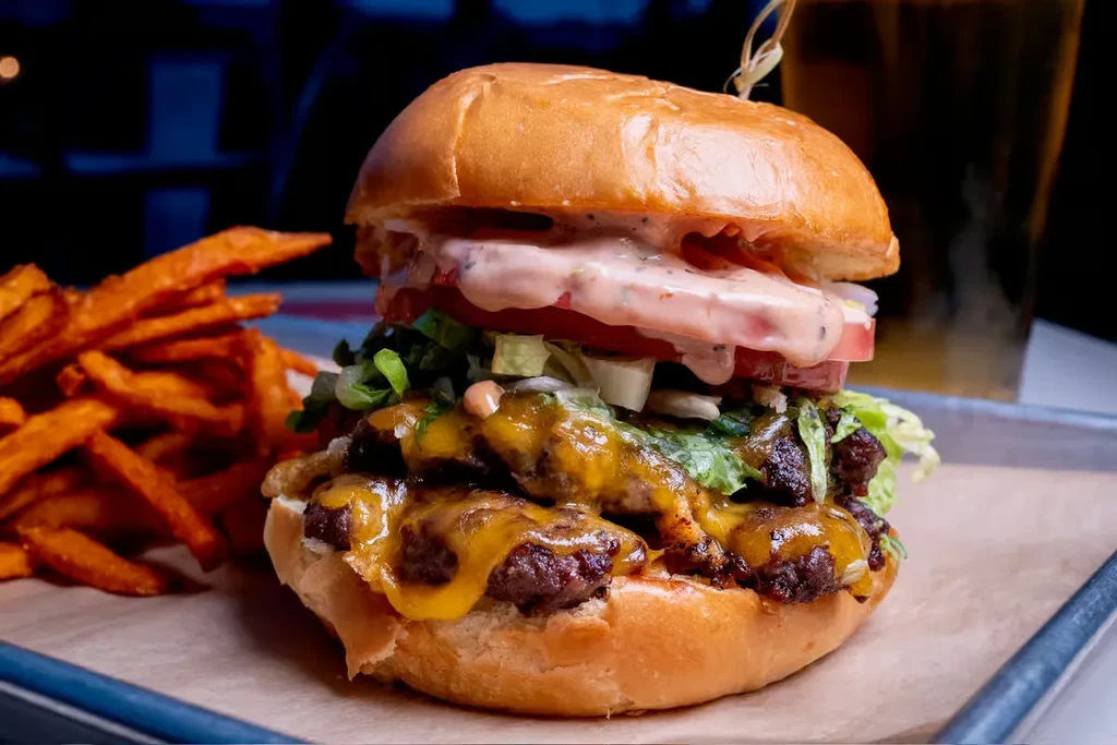 Double cheeseburger with sweet potato fries on parchment paper.