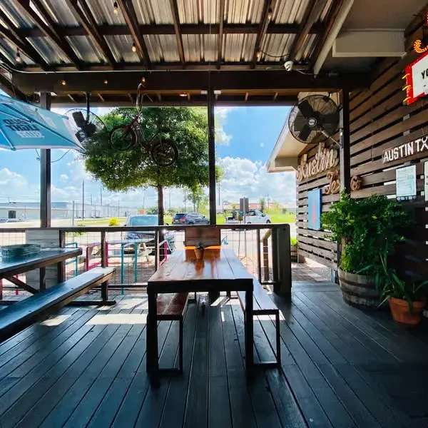 Casual restaurant patio with wooden tables, umbrella, and Austin signs.