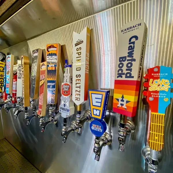 Close-up of numerous colorful beer taps with various brand names.