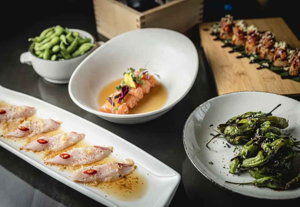 Assortment of Japanese dishes with sashimi, shishito peppers, and sushi.