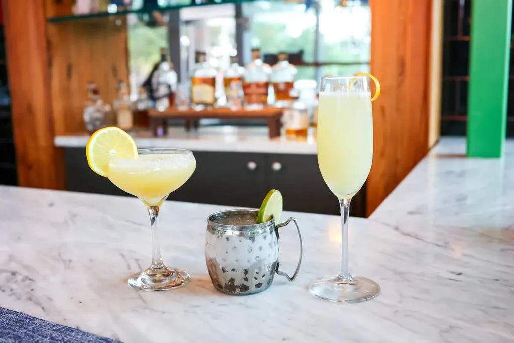 Three drinks in various glasses on a white marble bar top.
