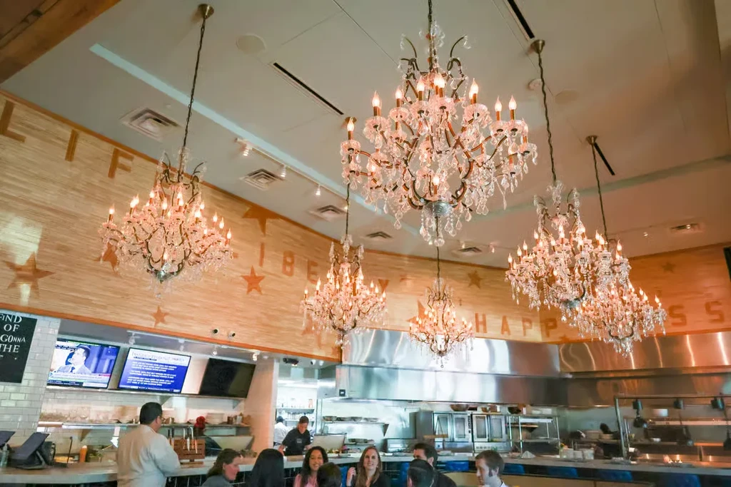 Restaurant interior with chandeliers, Americana decor, and patrons at a bar.