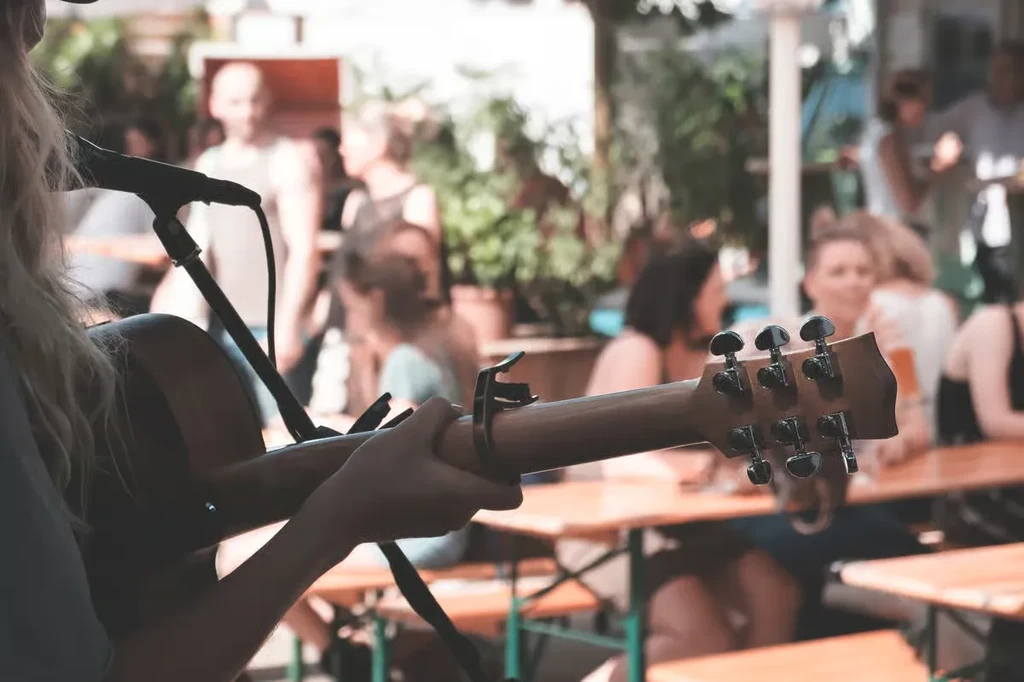 Person with blonde hair playing acoustic guitar with capo outdoors.