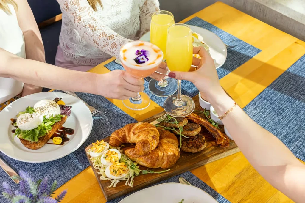 Three people toasting with mimosas and cocktails at a brunch table.