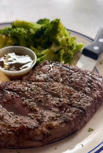 Well-cooked steak, broccoli, and sauce on a white plate.