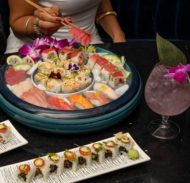 Sushi and sashimi platter with orchids, lemon, and a cocktail.