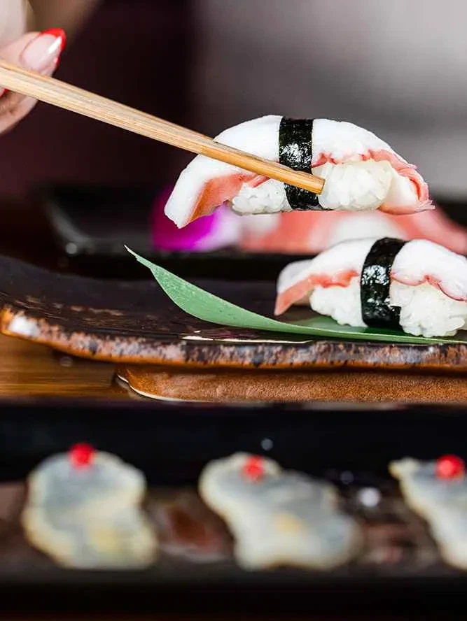 Nigiri sushi with white fish or octopus held by chopsticks.