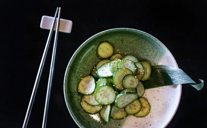 Bowl of sliced cucumbers with sesame seeds and chopsticks.