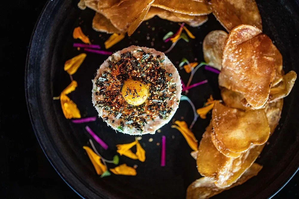 Tartare with egg yolk, chips, flower petals, and purple garnish.