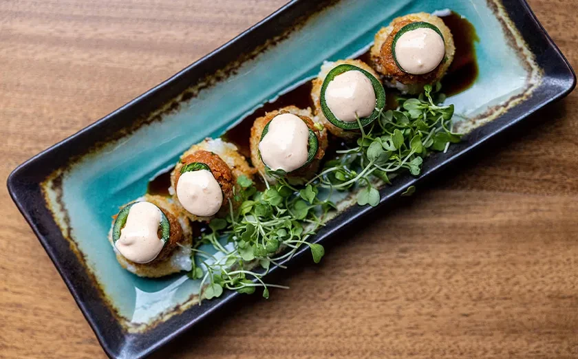 Five fried rolls with jalapeño and sauce on a teal dish.