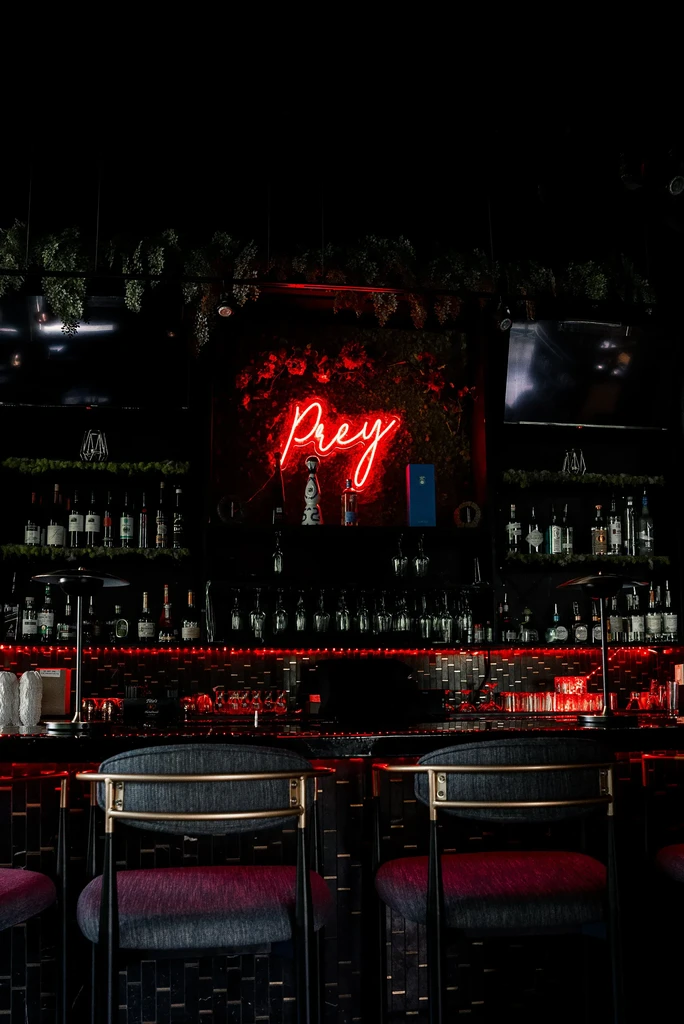 Dimly lit bar with a red neon "Prey" sign above the counter.