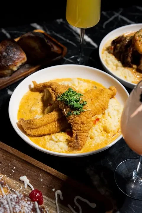 Fried fish and creamy sauce, drinks, and bread on a dark tabletop.