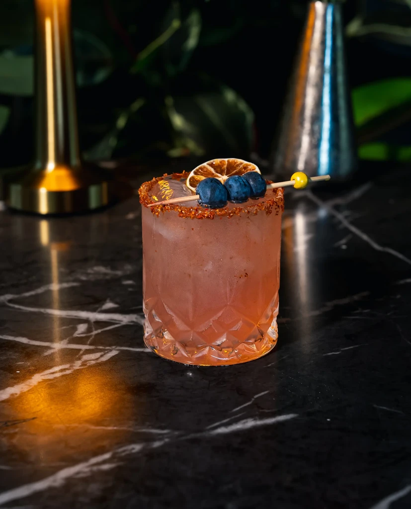 Reddish-pink cocktail in a textured glass with fruit garnish.