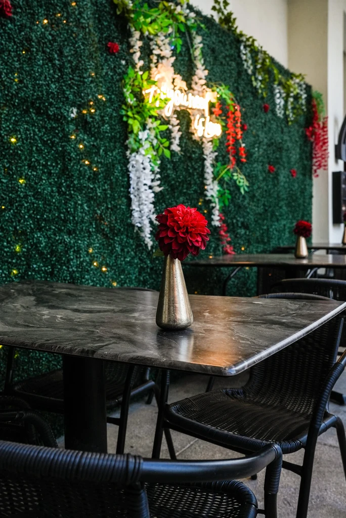 Restaurant seating area with tables, chairs, flowers, and a neon sign.