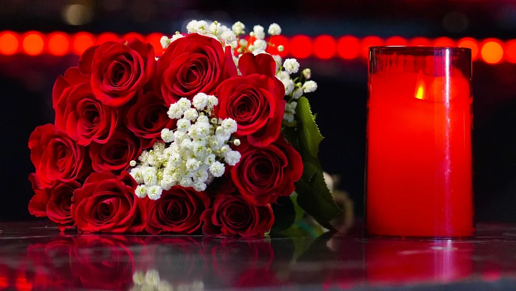 Red roses, baby's breath, and a lit candle on a dark surface.