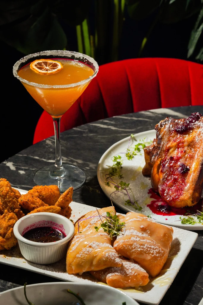 Beignets, French toast, and a cocktail on a dark marble table.