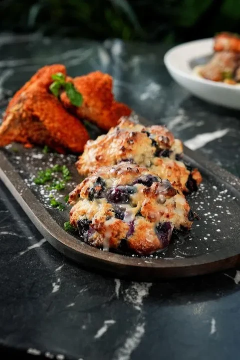 Three blueberry scones with glaze, garnished with herbs and powdered sugar.
