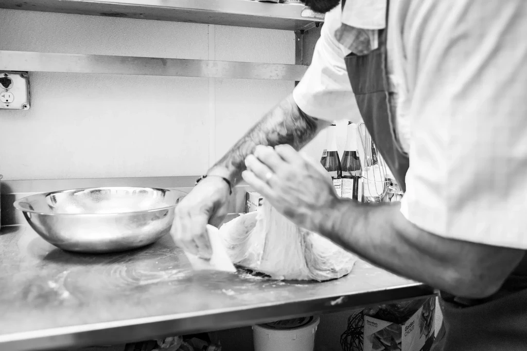 Hands kneading dough on a stainless steel surface in a kitchen.