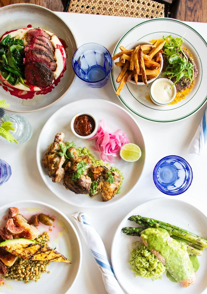 Overhead shot of five gourmet dishes and drinks on a white table.