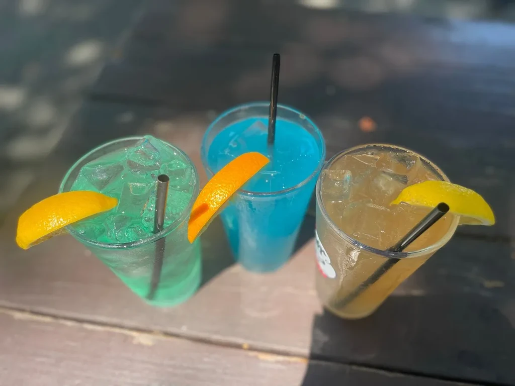 Three vibrant, iced drinks sit on a dark wooden table outdoors.