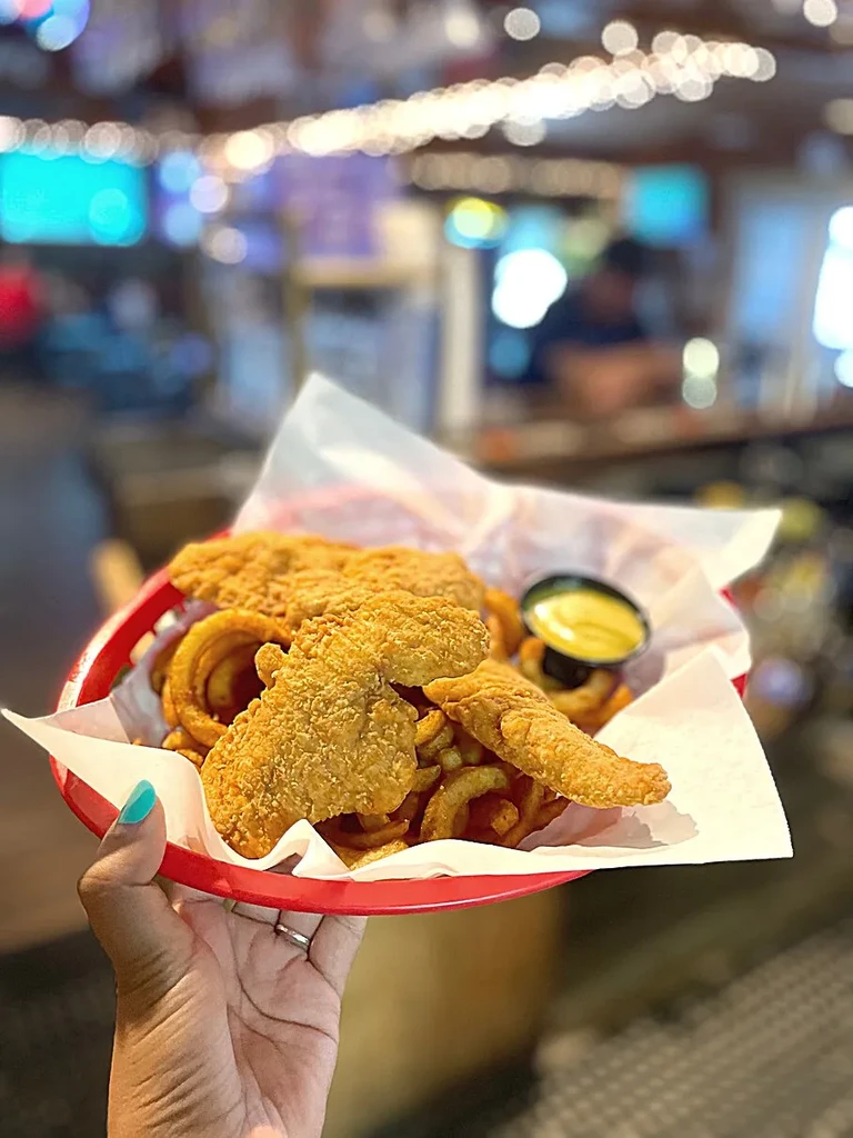 Fried chicken tenders, curly fries, and sauce in a red basket.