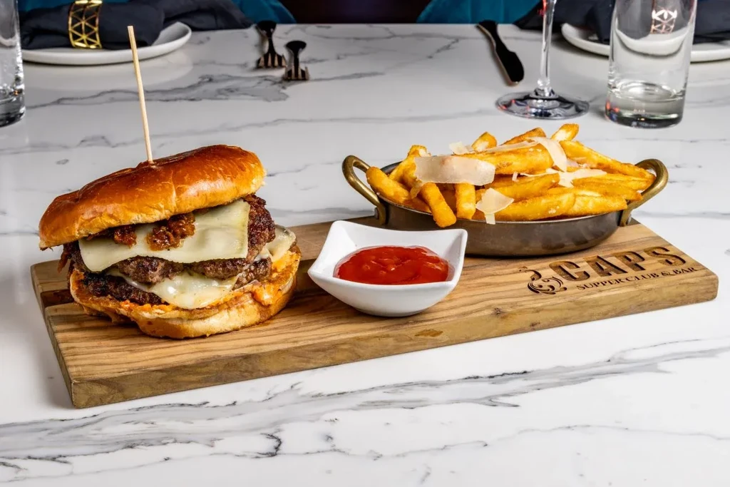 Double cheeseburger, parmesan fries, and ketchup on a wooden board.