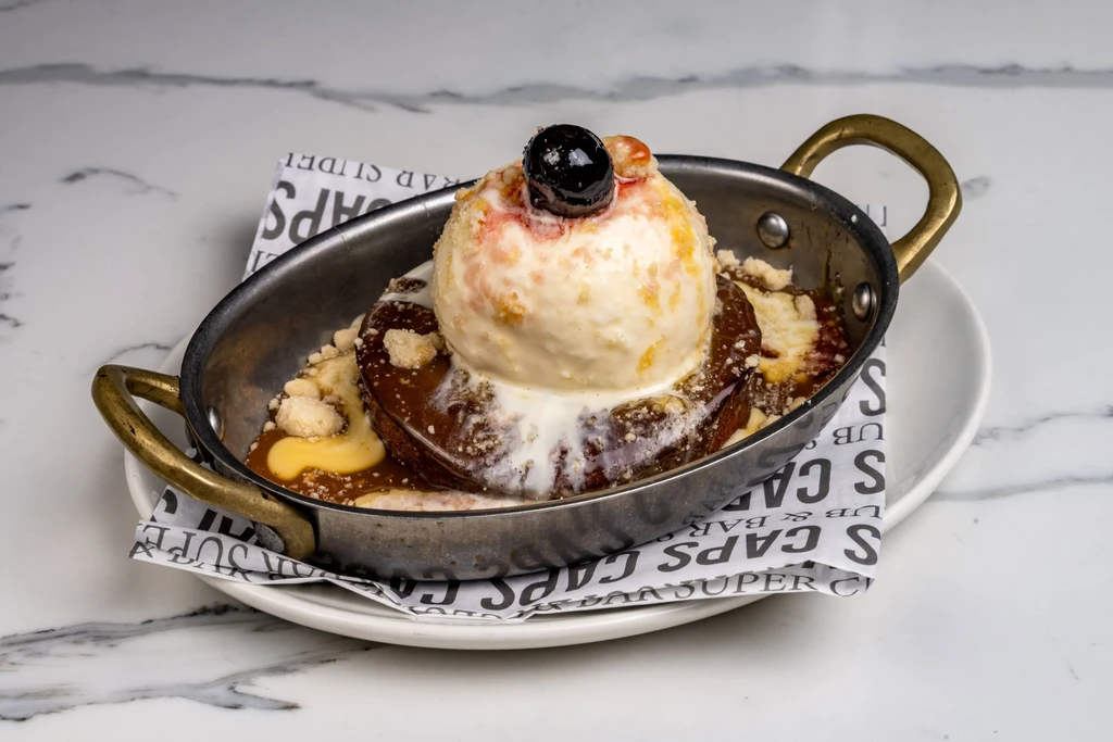 Dessert in metal pan with melting ice cream, cherry, and drizzle.