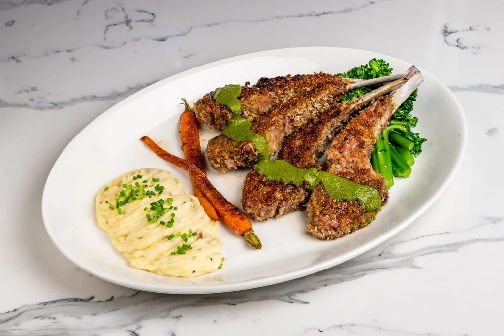 Lamb chops with green sauce, mashed potatoes, carrots, and broccoli.