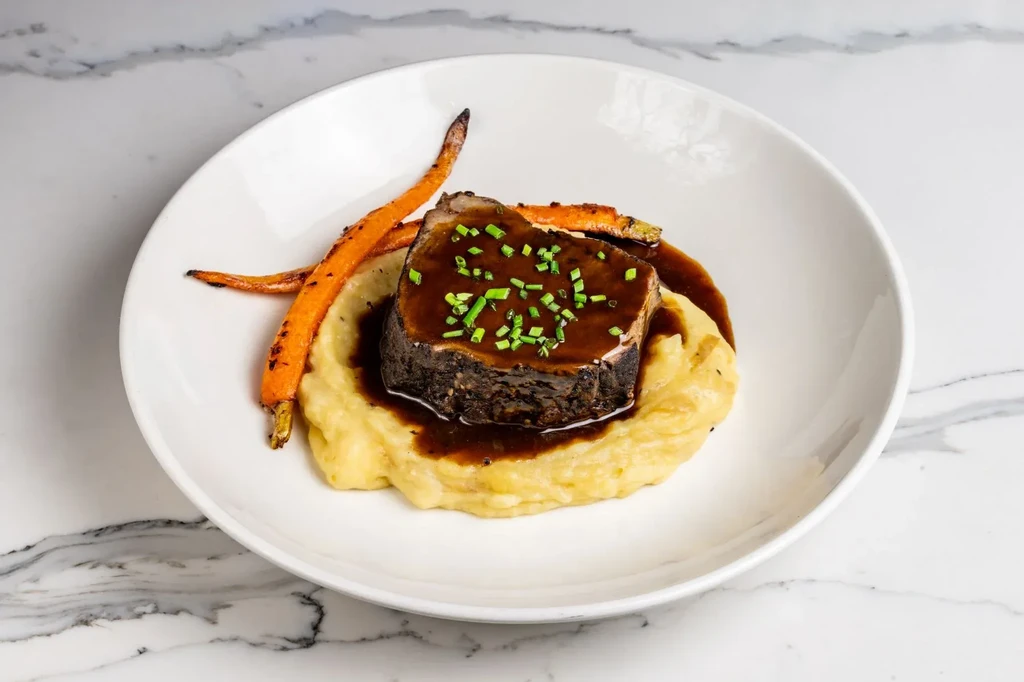 Braised short rib, mashed potatoes, and carrots on a white plate.