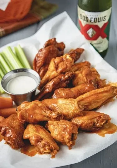 Plate of Buffalo chicken wings, dressing, vegetables, and beer.