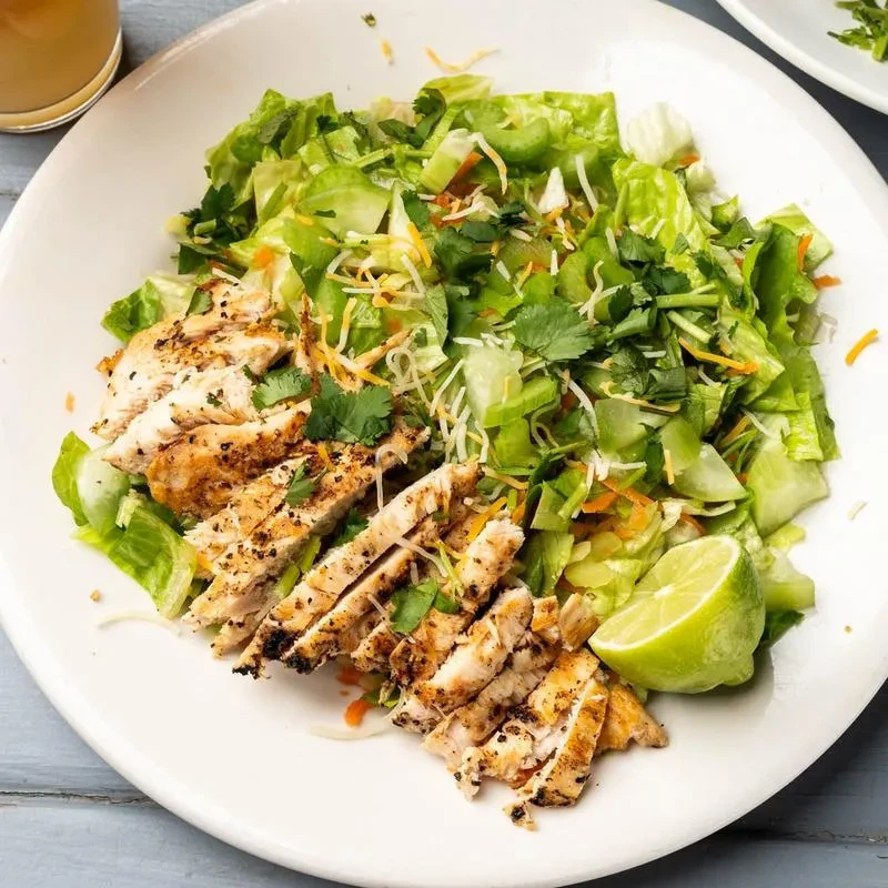 Overhead shot of grilled chicken salad with lime wedge.