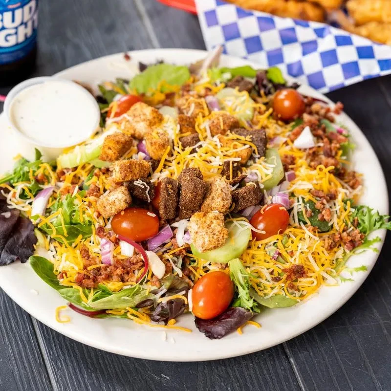 Large colorful salad with dressing, bacon, croutons, and cheese.