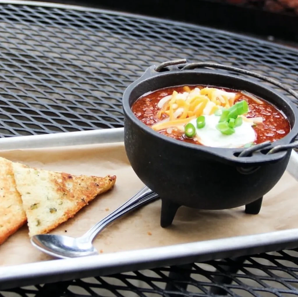 Chili in a cast iron pot with cheese, sour cream, green onions.
