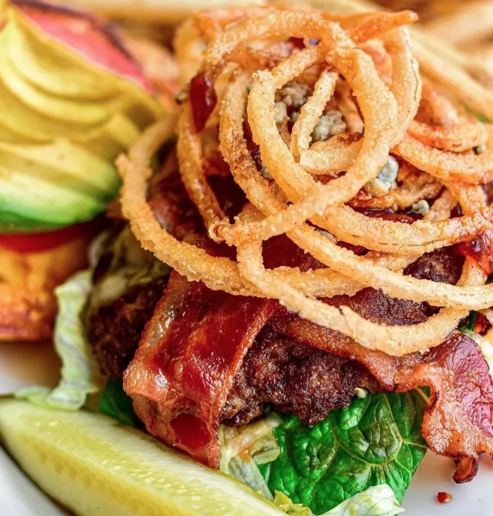 Gourmet burger with bacon, fried onion rings, blue cheese, and avocado.