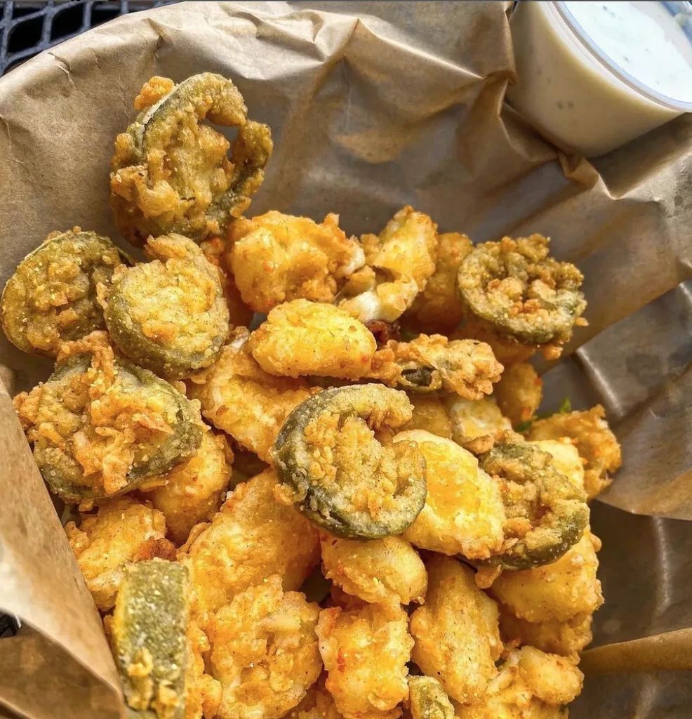 Close-up of fried pickles, cheese curds, and dipping sauce in a basket.