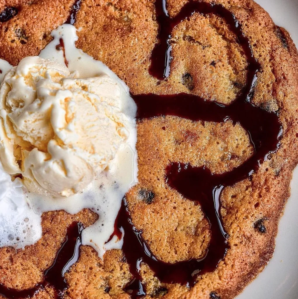 Warm chocolate chip cookie with melting vanilla ice cream and sauce.